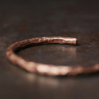 Hammered copper cuff lying on a dark stone surface