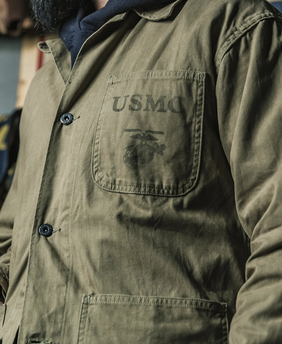 Close view of the jacket worn, showing the chest pocket stencil and metal buttons
