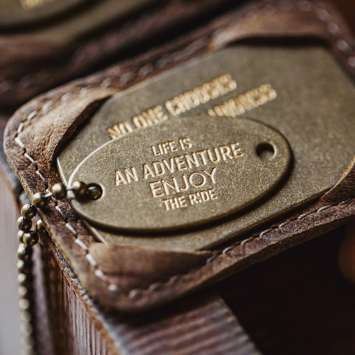 Macro of the oval brass tag engraved Life is an adventure, enjoy the ride, in the leather holder