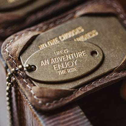 Macro of the oval brass tag engraved Life is an adventure, enjoy the ride, in the leather holder