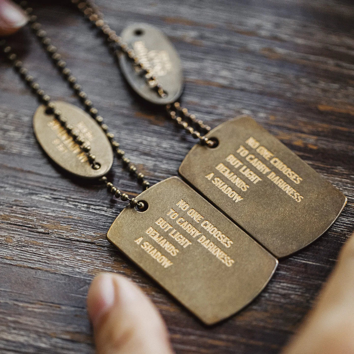 The two brass tags out of the holder on a wooden table, showing the engraved quotes