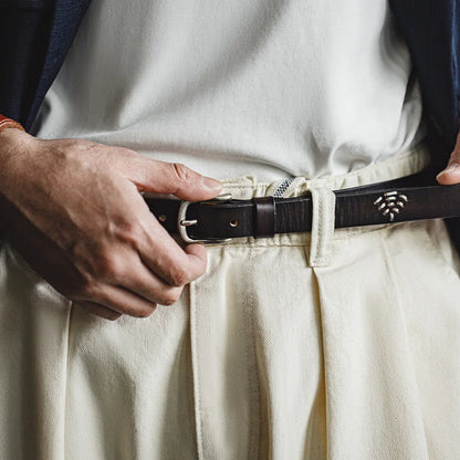 Slim black leather belt worn with pleated cream trousers, hands adjusting the buckle